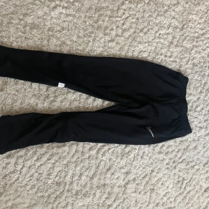 Svarta träningsbyxor från Nike - Säljer ett par svarta träningsbyxor från Nike i storlek 158-170 cm. Byxorna är tillverkade i ett lätt och bekvämt material med Dri-FIT-teknologi som håller dig torr under träningen. Perfekta för gymmet eller löprundan! Helt nya säljer pga inte min storlek. 