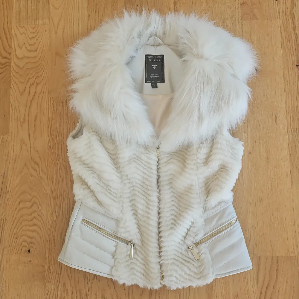 Säljer en superfin cremefärgad pälsväst från Guess i mycket bra skick. Västen har en fluffig krage och dragkedjor framtill. Perfekt för höst och vinter för att hålla sig varm och stilren. Passar både till vardags och festliga tillfällen.. Takit.
