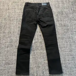 Säljer ett par svarta jeans från Nudie Jeans Co i mycket bra skick. De har en slim passform och är perfekta för både vardag och fest. Jeansen har klassiska fem fickor och knappgylf. Materialet är av hög kvalitet och ger en snygg och stilren look. 