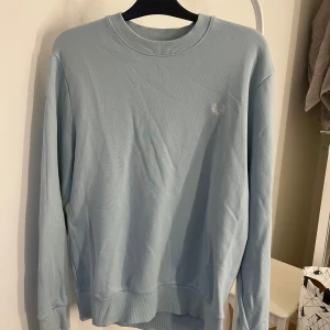 Ljusblå tröja från Fred Perry - Säljer en stilren ljusblå tröja från Fred Perry i storlek L. Tröjan är i mycket bra skick och har en klassisk design med ribbad krage och ärmslut. Perfekt för både vår och höst!