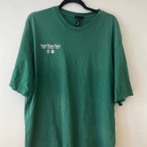 Grön t-shirt från H&M - Säljer en grön t-shirt från H&M i storlek L. Den har texten 'Never Waste Talent' tryckt både fram och bak. T-shirten är i bomull och har en avslappnad passform, perfekt för vardagsbruk. Den är kortärmad och i mycket bra skick.
