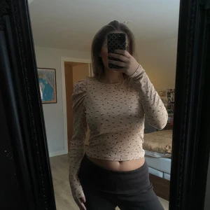 Beige långärmad topp från Monki - Säljer en superfin beige långärmad topp från Monki med små blommor. Den har en tight passform och är perfekt för både vår och höst. Toppen är i mycket bra skick och har en ribbad struktur som ger en extra touch. Perfekt för att styla med jeans eller kjol! 🌸