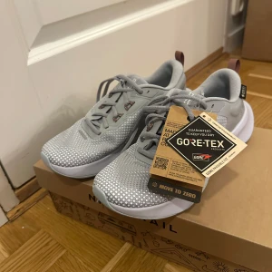 Grå Nike sneakers med Gore-Tex - Säljer ett par grå Nike sneakers i nytt skick. De har Gore-Tex för att hålla fötterna torra och är perfekta för träning. Skorna har snörning och en bekväm sula för bra grepp. De är stilrena och passar till både vardag och sportiga aktiviteter.