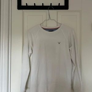Vit tröja från GANT - Säljer en stilren vit tröja från GANT i storlek S. Tröjan har långa ärmar och en klassisk rund halsringning med röd och svart randig detalj på insidan. Tröjan är använd 1 gång då den är för liten 🤍🥰