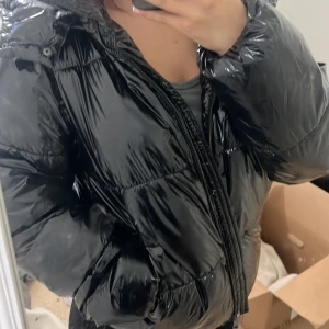 Svart glansig pufferjacka från Nelly - Säljer en svart glansig pufferjacka från Nelly i storlek M. Jackan har en dragkedja framtill och är perfekt för kalla dagar. Den är långärmad och har en modern look som passar både till vardags och fest. Superbekväm och håller dig varm hela vintern! 🖤Har haft jackan i någon vecka, priset går att diskutera :)