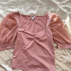Rosa topp med puffärmar  - Säljer en rosa topp. Den har korta puffärmar i ett transparent material med små prickar och en söt v-ringning. Perfekt för vår och sommar! 💖