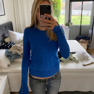 Blå tröja med knappar - Säljer en snygg blå tröja med långa ärmar och dekorativa knappar vid ärmsluten. Perfekt för både vardag och fest! Tröjan är i ett mjukt material. Hör av dig vid intresse! 💙