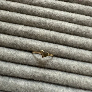 Guldfärgad ring med hjärta - Säljer en superfin guldfärgad ring med ett litet hjärta som detalj. Perfekt för att ge en subtil men söt touch till din outfit. Ringen är enkel och elegant, passar både till vardags och fest. Ett måste för alla som älskar minimalistiska smycken! 💛
