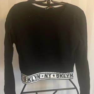 Ny Svart långärmad tröja från F&Sister - Säljer en svart långärmad tröja från F&Sister , på etiketten står det L men den är som en S-M.Den har en cool vit kant med texten 'BKLYN NY' runt nederkanten. Perfekt för en avslappnad stil eller en dag på stan. Tröjan är i ny skick och redo för nya äventyr!