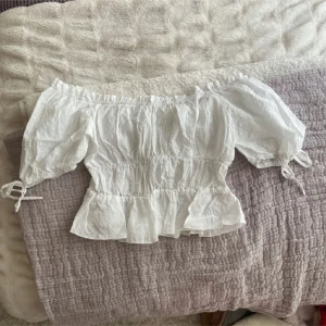 Vit offshoulder blus - Säljer en superfin vit offshoulder blus med volanger och knytband vid ärmarna. Perfekt för sommardagar eller en mysig vårutflykt. Blusen har en luftig och romantisk stil som passar både till vardags och fest. 🕊️