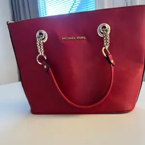 Säljer en snygg röd handväska från Michael Kors i skinn. Väskan har silverdetaljer och kedjehandtag som ger en lyxig känsla. Insidan är rymlig med flera fack och dragkedja för säker förvaring. Perfekt för både vardag och fest! 👜✨