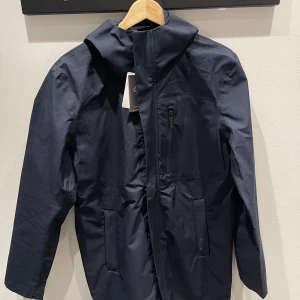 Mörkblå Carmel Car Coat från Berkeley - Säljer en snygg och funktionell mörkblå Carmel Car Coat från Berkeley. Jackan är vind- och vattentät med andningsbart material. Perfekt för höst och vår. Den har en dragkedja och en stilren design. Passar både till vardags och lite finare tillfällen.