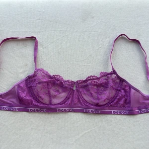 Lila spets-BH från Lounge - Säljer en superfin lila spets-BH från Lounge. Den har en elegant spetsdesign med justerbara axelband och en bekväm resår med Lounge-loggan. Perfekt för att känna sig både bekväm och snygg! 💜