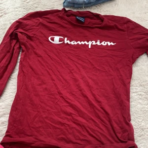 Röd långärmad tröja från Champion - Säljer en röd långärmad tröja från Champion med deras ikoniska logga tryckt på bröstet. Perfekt för en avslappnad stil. Tröjan är tillverkad i ett mjukt material som känns skönt mot huden.