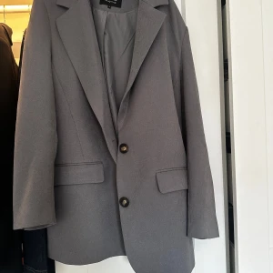 Grå kavaj från only  - Snygg grå kavaj från only med klassisk design och två knappar framtill. Perfekt för en stilren look. Kavajen har långa ärmar och två fickor med lock.