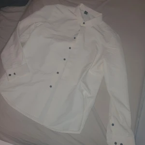Skjorta - Snygg vit/beige skjorta med svarta knappar. Perfekt för en stilren look. Skjortan har långa ärmar och en klassisk krage. Passar bra till både jeans och kostymbyxor. Aldrig använda!