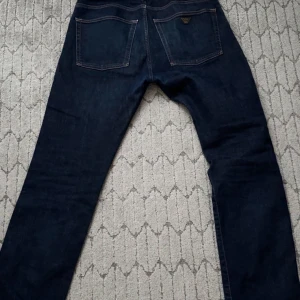 Mörkblå jeans från Emporio Armani (ÄKTA) - Snygga mörkblå jeans från Emporio Armani med klassisk femficksdesign och märkets logga på bakfickan. Jeansen har en rak passform och är perfekta för en stilren look. Tillverkade i högkvalitativt denim. Storlek 32x32 (nerklippta till ca längd 30).    ÄKTA