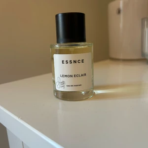 Essnce Lemon Eclair Eau de Parfum - Fräsch och uppfriskande parfym från Essnce med doft av citron. Flaskan är genomskinlig med en enkel design och svart kork. Perfekt för den som älskar citrusdofter.