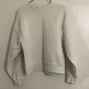 Vit sweatshirt - Säljer en stilren vit sweatshirt med rund hals och långa ärmar. Perfekt för en avslappnad look. Den har ribbade muddar vid ärmslut och nederkant för extra komfort.