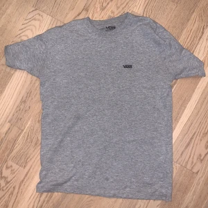 Grå t-shirt från Vans - Säljer en klassisk grå t-shirt från Vans i storlek small. Den är tillverkad av 90% bomull och 10% polyester, vilket gör den både bekväm och hållbar. Perfekt för en avslappnad stil med Vans-loggan diskret placerad på bröstet.
