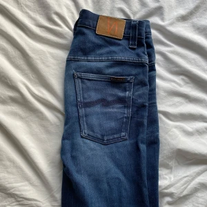 Blå jeans från Nudie Jeans - Snygga blå jeans från Nudie Jeans med klassisk femficksdesign och en bekväm passform. De har en tydlig logga på baksidan och en lätt slitning för en cool look. Perfekta för en avslappnad stil.