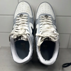 Vita och grå sneakers med snörning - Snygga vita och grå sneakers med snörning och perforerade detaljer på tån. Skorna har en stilren design med en kontrasterande svart detalj på sidan. Perfekta för en casual look.
