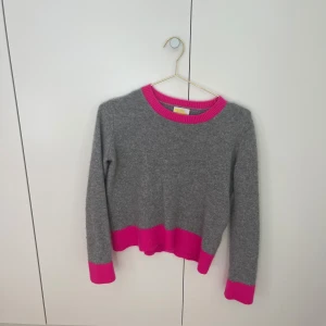 Grå och rosa kashmirtröja från From Future - Säljer en snygg grå kashmirtröja från From Future med rosa ribbade detaljer vid hals, ärmslut och nederkant. Tröjan har en klassisk rund hals och långa ärmar. Perfekt för att liva upp garderoben med lite färg! Köpte för 1000kr och säljer därför för 700kr