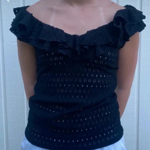 Svart offshoulder topp med volang - Snygg svart offshoulder topp med volangdetaljer. Perfekt för en somrig look. Toppen har ett hålmönster som ger en extra touch.