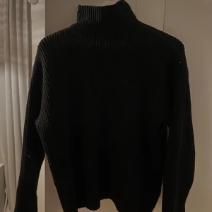 Svart ribbad polotröja från H&M - Säljer en stilren svart ribbad polotröja från H&M. Perfekt för kyligare dagar med sin höga krage och långa ärmar. Tröjan är i storlek M och passar utmärkt för en elegant och bekväm look.
