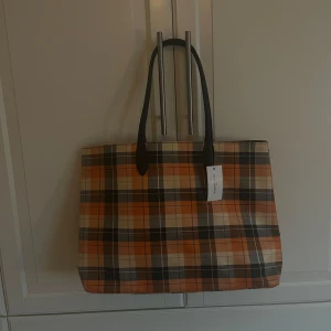 Rutig totebag - Snygg och rymlig shoppingväska med ett klassiskt rutigt mönster i orange, beige och svart. 