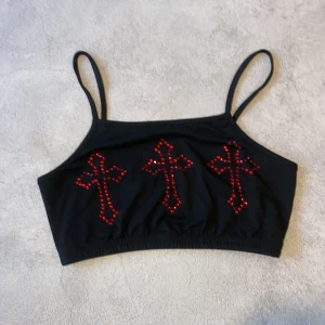 Svart topp med röda kors av diamanter  - Snygg svart topp med smala axelband och tre röda korsdetaljer framtill. Perfekt för en unik och edgy stil.