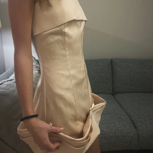 Champagnefärgad klänning från PrettyLittleThing - Snygg champagnefärgad klänning från PrettyLittleThing med en axelbandslös design😍perfekt till fest 