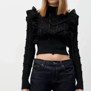 Svart croppad tröja med spetsdetaljer - Snygg svart croppad tröja med spetsdetaljer och volanger. Tröjan har långa ärmar och en tight passform, perfekt för en trendig look.
