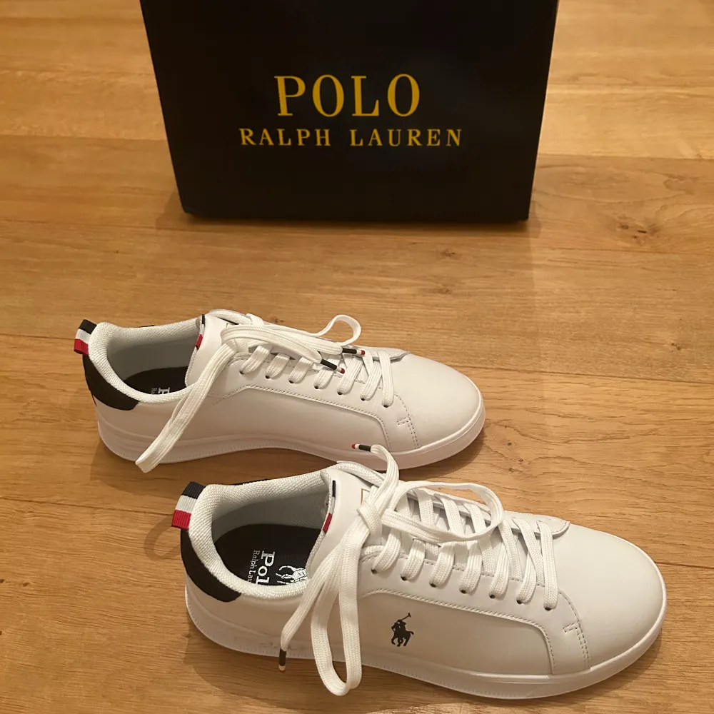 Aldrig använda med lappar kvar! As snygga vita sneakers från Polo Ralph Lauren med klassisk design. Skorna har snörning och en diskret logga på sidan. De har en vit sula och detaljer i rött, guld och blått på hälen i mocka. Perfekta för en stilren look. Har fysiskt och digitalt kvitto. Nypris 1595:-. Pris kan diskuteras vid snabb affär! Passa på nu när det är gratis frakt. Kengät.