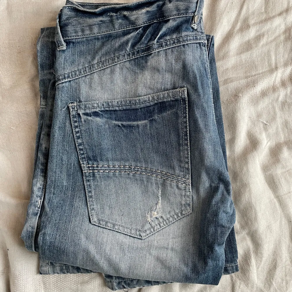 Snygga blå jeans från 98-86 Brand med unika dragkedjedetaljer på fickorna. De har en bootcut-stil och är perfekta för en avslappnad look. Märkesloggan är broderad på baksidan.. Farkut & Housut.