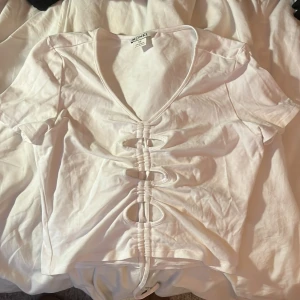 Vit kortärmad topp från Monki - Säljer en vit kortärmad topp från Monki, som har en dragsko på mitten av tröjan. Den är endast använd fåtal gånger, därav väldigt bra skick! 