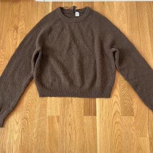 Brun stickad tröja från H&M Divided - Säljer en mysig brun stickad tröja från H&M Divided. Tröjan är långärmar och har ett häng band. Perfekt för kyligare dagar! Är använd bara två gånger.