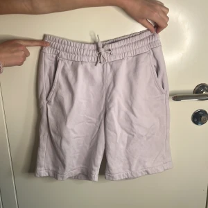 Ljuslila shorts från Kappa - Säljer ett par ljuslila shorts från Kappa med elastisk midja och snörning. Shortsen har två sidofickor och en bakficka med en liten broderad detalj. Perfekta för en avslappnad stil.