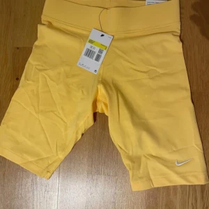 Gula träningsshorts från Nike - Snygga gula träningsshorts från Nike i en tight passform. Perfekta för sommarens alla träningspass. De har en elastisk midja för extra komfort och en liten Nike-logga på benet.