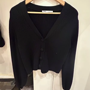 Svart kofta från Zara - Säljer en stilren svart kofta från Zara med v-ringning och knappar framtill. Koftan har långa ärmar och är perfekt för kyligare dagar. Passar bra till både jeans och kjol.