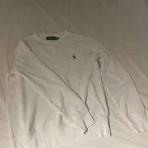 Vit tröja från Polo Ralph Lauren - Säljer en klassisk vit tröja från Polo Ralph Lauren med deras ikoniska logga broderad på bröstet. Tröjan har långa ärmar och en rund halsringning. Perfekt för en stilren look.