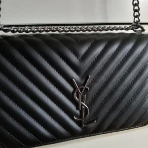 Helt ny väska  - Ej äkta YSL. Snygg svart axelväska med quiltat mönster och kedjerem. Väskan har en elegant design med metallogo framtill. Perfekt för att ge din outfit en lyxig touch.