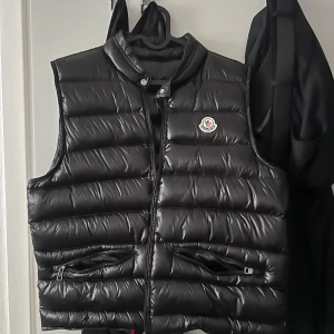 Moncler väst S - Snygg svart dunväst från Moncler med dragkedja och två fickor framtill. Perfekt för kyligare dagar och ger en stilren look. Moncler-logga på bröstet. INGA SKADOR 