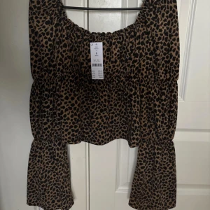 Leopardmönstrad topp från Gina Tricot - Snygg leopardmönstrad topp från Gina Tricot med långa ärmar och en luftig passform. Perfekt för att ge din outfit en trendig vibe. Toppen har en elastisk halsringning och är tillverkad i ett mjukt material. Har enbart testats. 