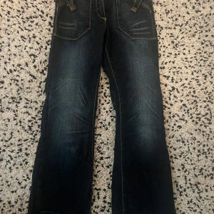 Mörkblå jeans med broderade bakfickor - Snygga mörkblå jeans med coola broderade detaljer på bakfickorna. De har en klassisk femficksdesign och en lätt utsvängd bootcut-stil. Perfekta för en avslappnad look. Storlek 140🤍