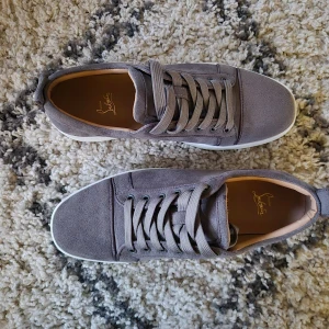 Grå sneakers från Christian Louboutin. Storlek 42 - Snygga grå sneakers i mocka från Christian Louboutin med den ikoniska röda sulan. Skorna har snörning och en stilren design som passar perfekt för en trendig look. Storlek 42