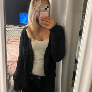 Svart kofta med knappar - Säljer en svart kofta med knappar framtill. Den har en ribbad struktur och långa ärmar, perfekt för kyligare dagar. Koftan är stilren och lätt att matcha med olika outfits. Storlek L men skulle säga att den är mindre