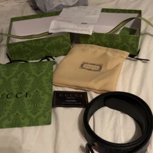 Svart bälte med Mickey Mouse från Gucci - Snyggt svart bälte från Gucci med ett unikt Mickey Mouse-motiv. Bältet har en GG-logotyp som spänne och är tillverkat i Italien. Perfekt för att ge din outfit en lekfull touch! Fick det i julklapp, vet ej om det är äkta men tror det,, säljer pga att ja behöver pengar