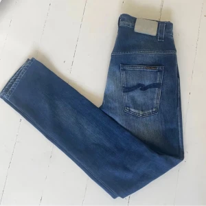 Blå jeans från Nudie Jeans - Snygga blå jeans från Nudie Jeans med en klassisk femficksdesign. De har en slimfit / regular passform och är tillverkade i slitstarkt denim. Perfekta för en avslappnad stil.