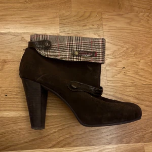 Bruna mocka boots med rutigt skaft - Snygga bruna mocka boots med en unik rutig detalj på skaftet. Skorna har en klack och en dekorativ rem över foten. Inga större defekter, små i storlek